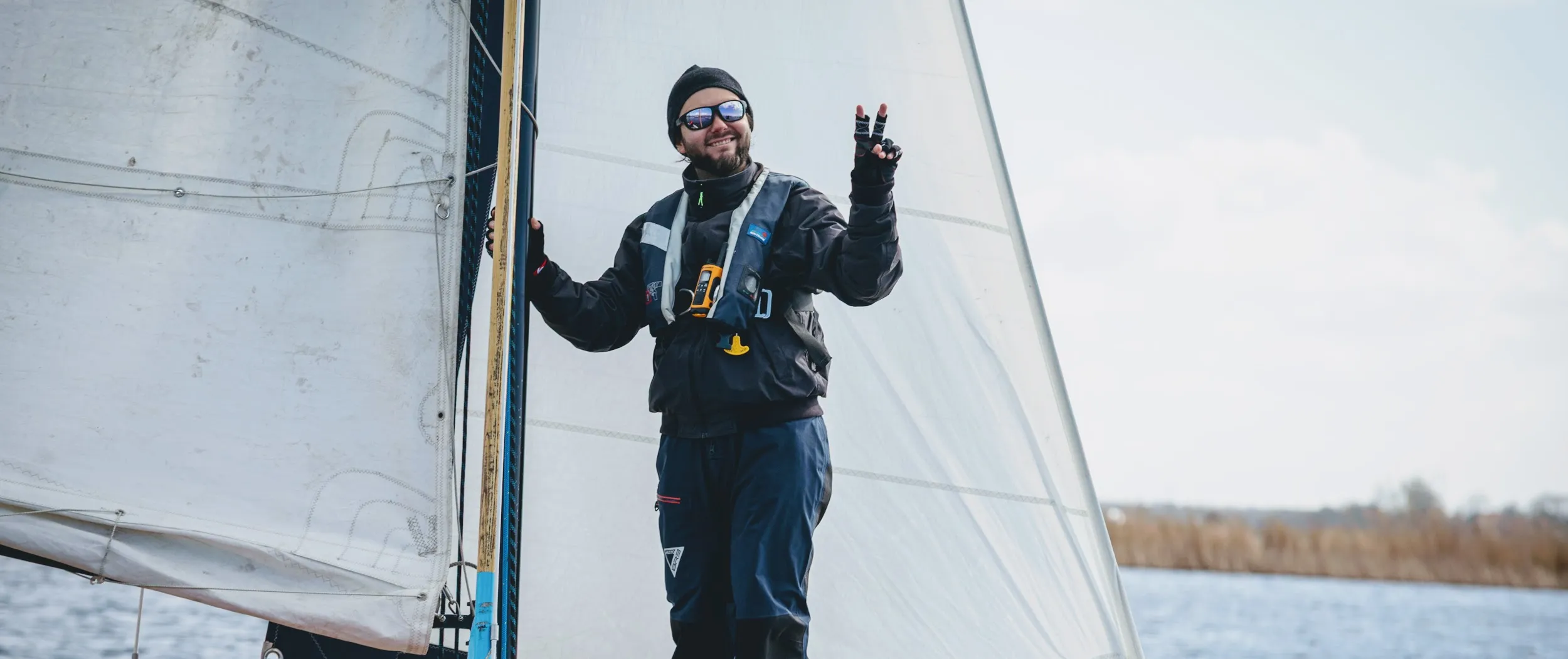 Marvin Strangfeld on a sailboat flashing a peace sign, sails up on open water.